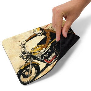 May include: A vintage-style illustration of a person riding a motorcycle. The illustration is in shades of yellow, brown, red, and black, and has a distressed, aged look. The motorcycle has a large front wheel and a smaller rear wheel. The person is wearing a helmet and a brown jacket.
