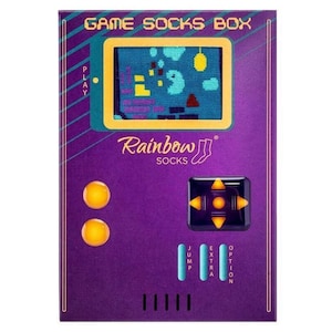 Könnte beinhalten: Eine violette und türkisfarbene Box mit dem Text "GAME SOCKS BOX" und "Rainbow Socks" darauf. Die Box ist so gestaltet, dass sie wie eine Retro-Videospielkonsole aussieht, mit einem Bildschirm, der ein pixeliges Spiel zeigt. Die Box hat Knöpfe mit den Aufschriften "PLAY", "JUMP", "EXTRA" und "OPTION".