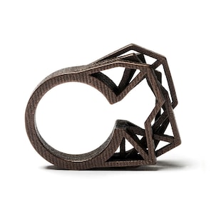 Könnte beinhalten: Ein bronzefarbener Ring mit geometrischem Design. Der Ring besteht aus mehreren übereinander gestapelten Metallschichten.