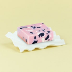 Pu&ograve; includere: Una saponetta rosa e nera macchiata su un piatto bianco ondulato.
