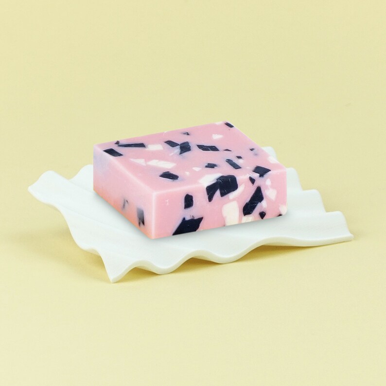 Pu&ograve; includere: Una saponetta rosa e nera macchiata su un piatto bianco ondulato.