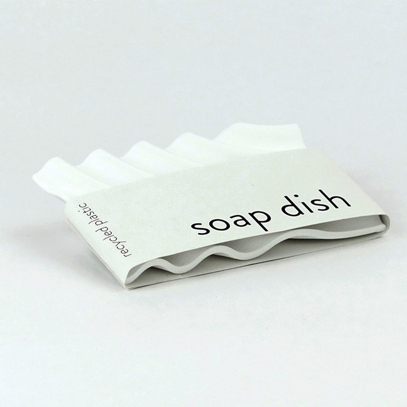 Pu&ograve; includere: Portasapone bianco in plastica riciclata con un bordo ondulato e la scritta "soap dish" stampata sul davanti.