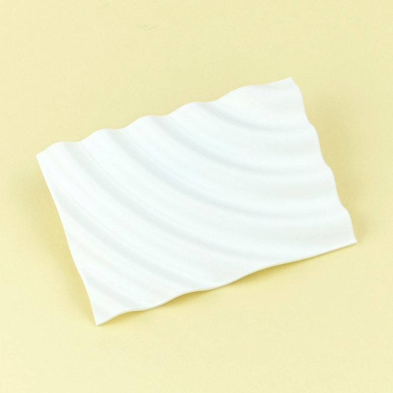 Pu&ograve; includere: Piatto rettangolare bianco in ceramica con una superficie ondulata.