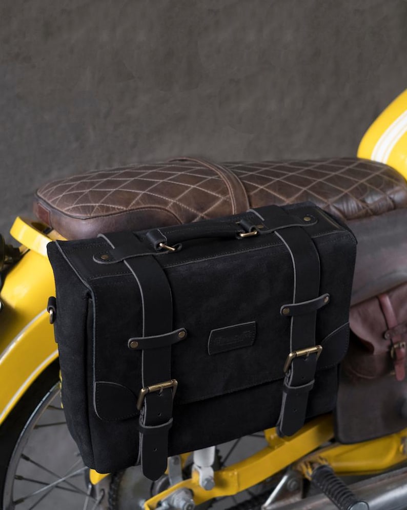 May include: Black leather motorcycle saddlebag with buckles and straps. The bag is attached to a yellow motorcycle.