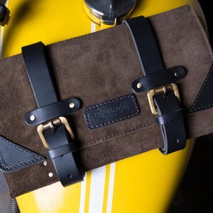 May include: Brown leather motorcycle tool roll with black straps and buckles. The roll has a black leather patch with the text "The Machine" embossed on it.
