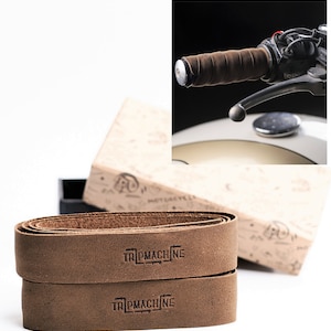 May include: Two brown leather handlebar tape rolls with the text "Tripmachine" embossed on each roll. The tape is designed for motorcycles.