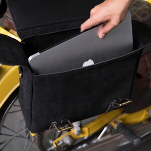 May include: A black leather motorcycle bag with a laptop inside. The bag has two buckles on the front and is attached to a yellow motorcycle.