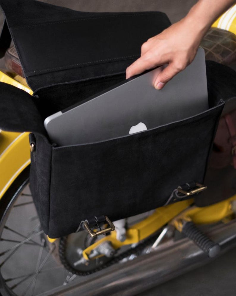 May include: A black leather motorcycle bag with a laptop inside. The bag has two buckles on the front and is attached to a yellow motorcycle.