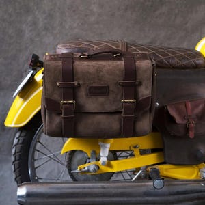May include: A brown leather motorcycle saddlebag with buckles and straps attached to a yellow motorcycle.