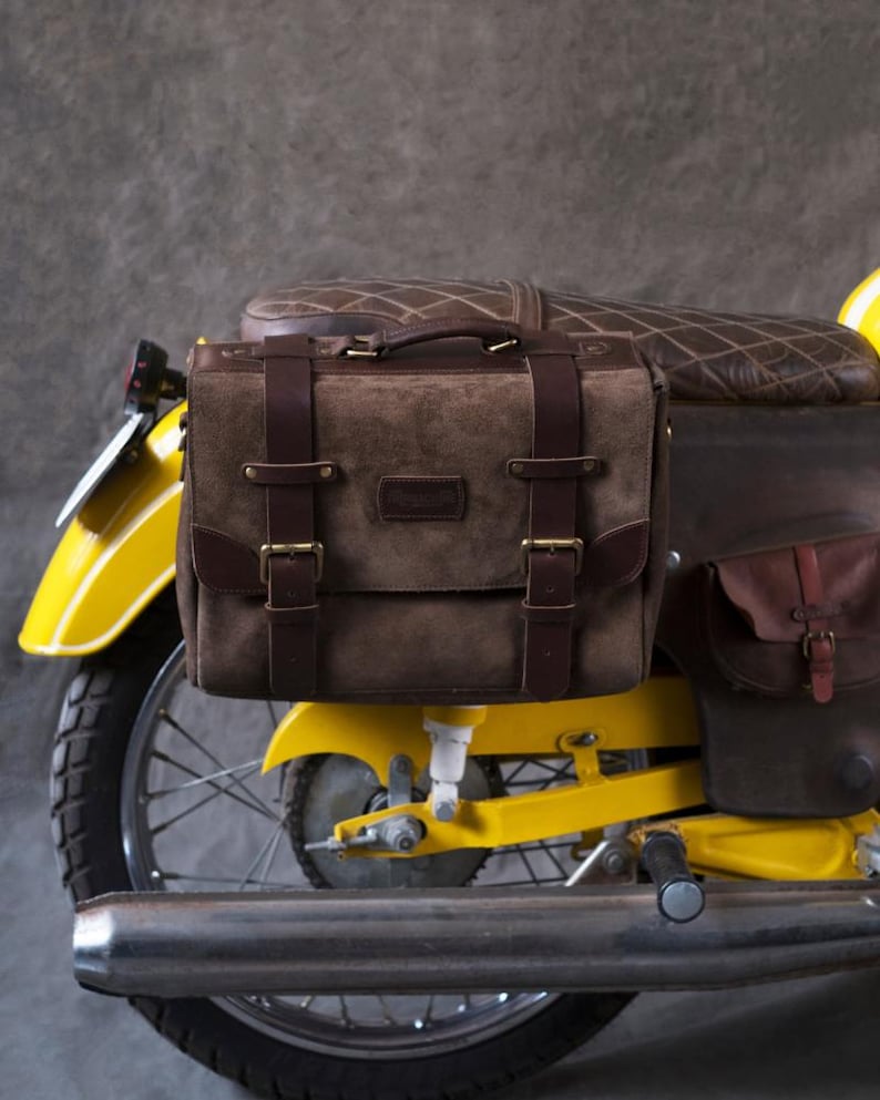 May include: A brown leather motorcycle saddlebag with buckles and straps attached to a yellow motorcycle.