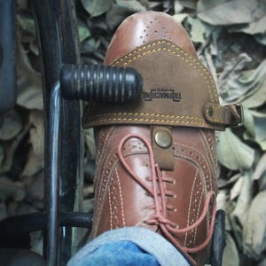 Könnte beinhalten: Braunes Leder-Motorradzubehör für den Fuß mit dem Text "Tripmachine" darauf.