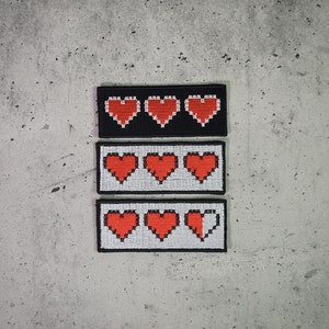 Könnte beinhalten: Drei pixelige Herz-Patches in einer Reihe, jeweils mit schwarzem oder weißem Hintergrund. Die Herzen sind rot und weiß, wobei ein Patch ein halb gefülltes Herz zeigt. Die Patches sind rechteckig.