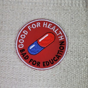 Może przedstawiać: Naszywka z haftowanym czerwonym i niebieskim pigułką z białym tekstem, który brzmi "Dobre dla zdrowia Złe dla edukacji".