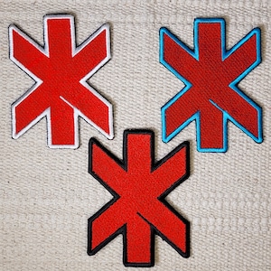 Può includere: Tre toppe a forma di stella rossa con contorni bianchi. La toppa superiore è bordata di blu. La toppa inferiore è bordata di nero.