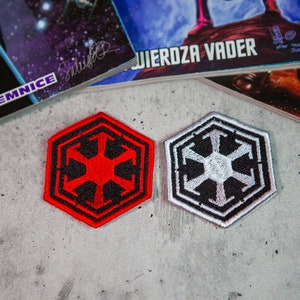 Op de afbeelding: Twee geborduurde strijkpatches met het symbool van het Galactische Keizerrijk uit Star Wars. Eén patch is rood met zwarte details, de andere is wit met zwarte details.