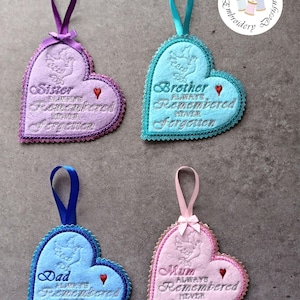 May include: Four heart-shaped embroidered ornaments with ribbon loops. Each ornament is a different color: purple, blue, light blue, and pink. The ornaments have text that reads "Sister", "Brother", "Dad", and "Mum", with the phrase "Always Remembered Never Forgotten".