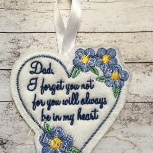 May include: White felt heart-shaped ornament with blue forget-me-not flowers and the text "Dad I forget you not for you will always be in my heart".