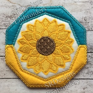 May include: A yellow sunflower embroidered on a white background with a teal blue border. The design is in the shape of an octagon and has the text "SRDesigns Embroidery" on the bottom.