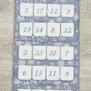 May include: A gray felt advent calendar with a white snowflake pattern. The top flap features a black silhouette of Santa Claus in a sleigh pulled by reindeer with the text "HO! HO! HO! Merry Christmas". The calendar has 24 numbered pockets.