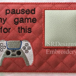 May include: Red quilted fabric with a white video game controller and the text "I paused my game for this". A white rectangle with the text "SRDesigns Embroidery" is in the upper right corner.
