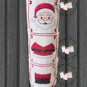 May include: A white Christmas-themed embroidered item featuring Santa Claus's face, jacket, and pants. The design includes red and black accents, with a decorative red border. The item is likely a decorative piece or a holiday-themed craft.