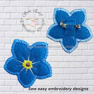 May include: Two blue flower-shaped embroidered patches with five petals and a yellow center. One patch shows the front with detailed stitching, while the other shows the back with a metal pin fastener. The text Sew Easy Embroidery Designs is visible.