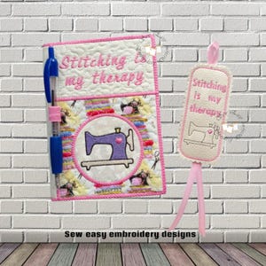 May include: A quilted notebook and bookmark set with the text "Stitching is my therapy." The notebook features a blue pen and a purple sewing machine design. The bookmark has a pink ribbon and a matching sewing machine illustration.