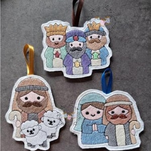 May include: Embroidered Christmas decorations depicting religious figures. The set includes three wise men, a shepherd with sheep, and Mary and Joseph. Each decoration has a ribbon for hanging. The decorations are made with various colours of thread.