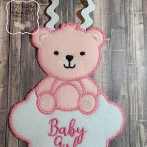 May include: Pink embroidered teddy bear sitting on a white cloud with the text "Baby Girl" in pink embroidery.