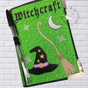 May include: A green notebook cover featuring embroidered designs of a black witch hat with yellow stars, a crescent moon, stars, and a broomstick. The word Witchcraft is embroidered in black at the top. A black pen is held in an elastic loop on the side.