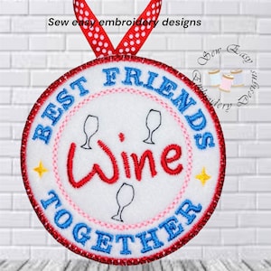 Könnte beinhalten: Gestickter runder Schmuck mit den Worten "BEST FRIENDS TOGETHER" in Blau und "Wine" in Rot. Mit Weingläsern und Sternen. Der Schmuck hat einen roten Rand und ein rot-weiß gepunktetes Band zum Aufhängen.