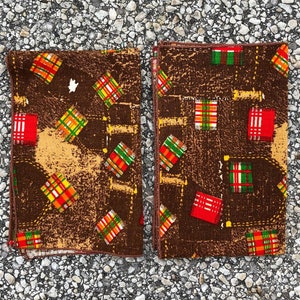 Könnte beinhalten: Zwei braune Stoff-Platzsets mit einem geometrischen Muster aus roten, grünen, gelben und weißen Quadraten. Die Platzsets haben einen Used-Look und einen braunen Hintergrund.