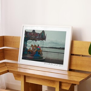 May include: A framed photograph of a carousel with colourful horses and a white roof. The carousel is on a pier overlooking a body of water. The text "Bournemouth Pier, Dorset, England" is written in cursive at the bottom of the photo.