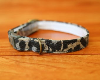 以下が含まれることがあります： 黒とタンのアニマルプリントデザインのペット用カラー。カラーは白い裏地、真鍮色の金属リング、緑色のプラスチックバックルが付いています。このカラーはペット用に設計されています。