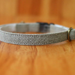 May include: A gray fabric cat collar with a metal buckle. The collar is made of a woven fabric with a subtle texture.