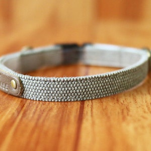 May include: A gray and white woven dog collar with a brown leather accent and a silver buckle.