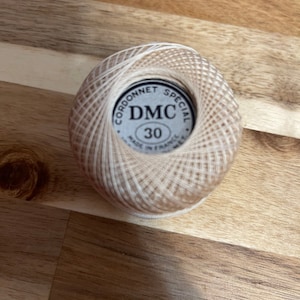 May include: A ball of white and beige embroidery floss with a brown label that reads "Cordonnet Special DMC 30 Made in France".