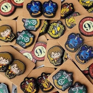 May include: A collection of small, colorful enamel pins featuring various designs including cartoon characters with glasses, house crests with animals, and circular red and white signs with the text Platform 9 3/4 Hogwarts Express.