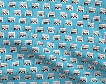 May include: A light blue fabric featuring a repeating pattern of white rectangular birthday cake illustrations, each topped with a single candle and the black text "BIRTHDAY BOY" printed clearly on the front of the cake graphic.