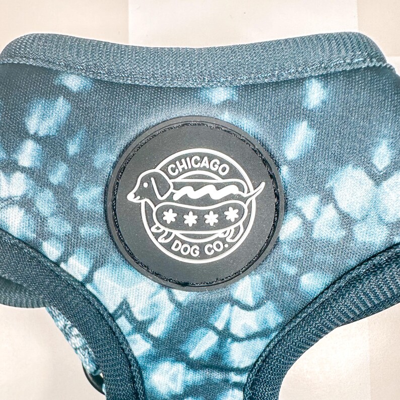 May include: A blue and white tie-dye dog harness with a black patch that says "Chicago Dog Co." and features a cartoon dachshund with a hot dog.
