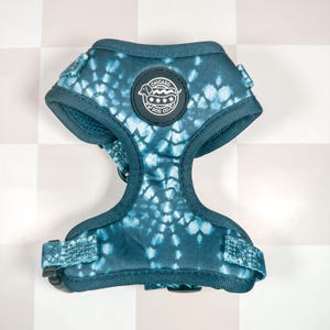 May include: A teal blue dog harness with a tie-dye pattern. The harness has a black buckle and a circular patch with the text "CHICAGO  PY DOG CO."