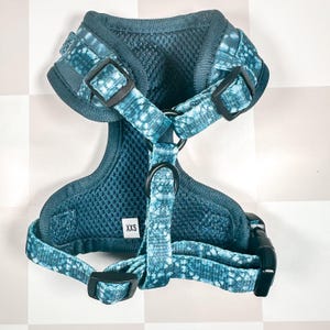 May include: A blue and black patterned dog harness with a mesh lining and adjustable straps. The harness has a size tag that says "XXS".