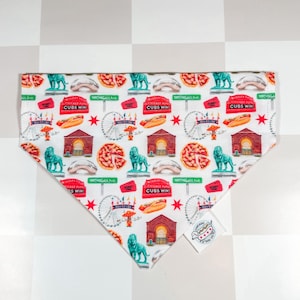 May include: White dog bandana with a repeating pattern of Chicago landmarks, including lions, pizza slices, Ferris wheels, and hot dogs. The bandana also features the text "Cubs Win!" and "Michigan Ave."