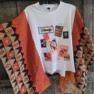 May include: A white t-shirt featuring a graphic print of various postage stamps, including one with a portrait of Dolly Parton, the word Howdy, and the text dolly dolly dolly. The shirt has wide, quilted sleeves in burnt orange with dark brown patterns.