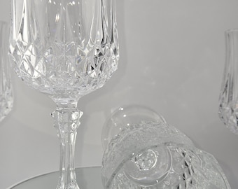 Könnte beinhalten: Klare Weingläser aus Kristall mit rautenförmigen Mustern. Ein Glas steht aufrecht, während ein anderes auf der Seite liegt. Die Gläser haben eine tulpenförmige Schale und einen detaillierten Stiel. Das Glas steht auf einer verspiegelten Oberfläche.