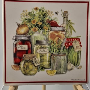 May include: A decorative ceramic tile featuring a still life of various preserved foods in glass jars. The image includes jars of pickles, beets, and peaches, along with fresh herbs, onions, and garlic. The tile has a red border.