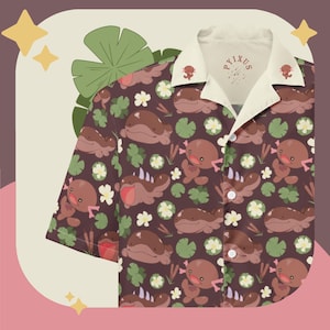 Puede incluir: Camisa marrón con botones con un patrón repetido de ajolotes de dibujos animados, nenúfares y flores. La camisa tiene un cuello blanco con el texto "PYXUS" y gráficos de ajolotes. La camisa es de manga corta y tiene un corte relajado.
