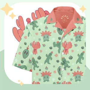 Op de afbeelding: Een lichtgroen overhemd met korte mouwen en een knoopsluiting, voorzien van een herhalend patroon van diverse groene en roze cactusillustraties en kleine witte sterren. Het overhemd heeft een effen koraalkleurige kraag en de tekst PYIXUS.