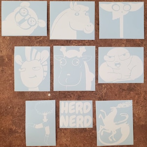 May include: Nine white vinyl stickers featuring cartoon characters and text. The stickers include a giraffe, a horse, a creature with large eyes, a creature with a large head, a creature with a large body, a creature with a tree on its head, a creature with a tail, and the text "Herd Nerd".