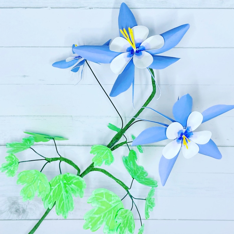 May include: A blue and white paper flower with green leaves. The flower has five petals and a yellow center. The leaves are arranged around the flower.